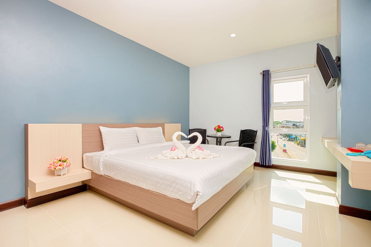 Una habitación de hotel moderna con una cama grande, una mesita con un florero, un televisor montado en la pared y vistas de la ciudad a través del ventanal.