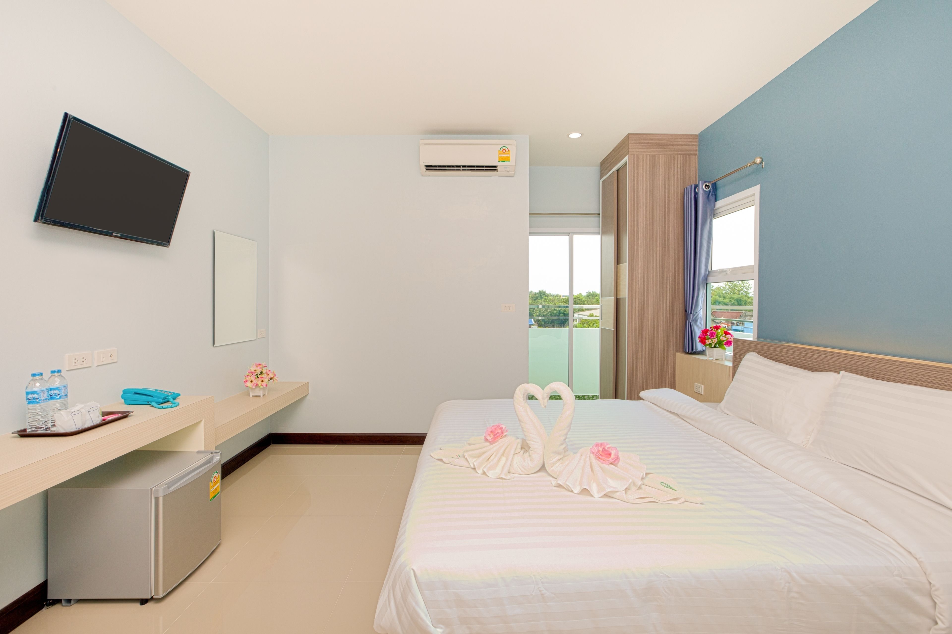 A hotel room with a bed, a desk, a television, and an air conditioning unit.