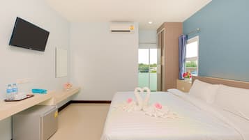 A hotel room with a bed, a desk, a television, and an air conditioning unit.