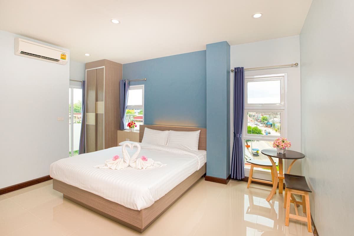 Habitación de hotel con cama, una mesita, una silla, equipo de aire acondicionado y una ventana con cortinas.