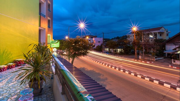 A street view at dusk with a brightly lit building on the left and a road with light trails indicating traffic. - Je t'aime Hotel (Trang)