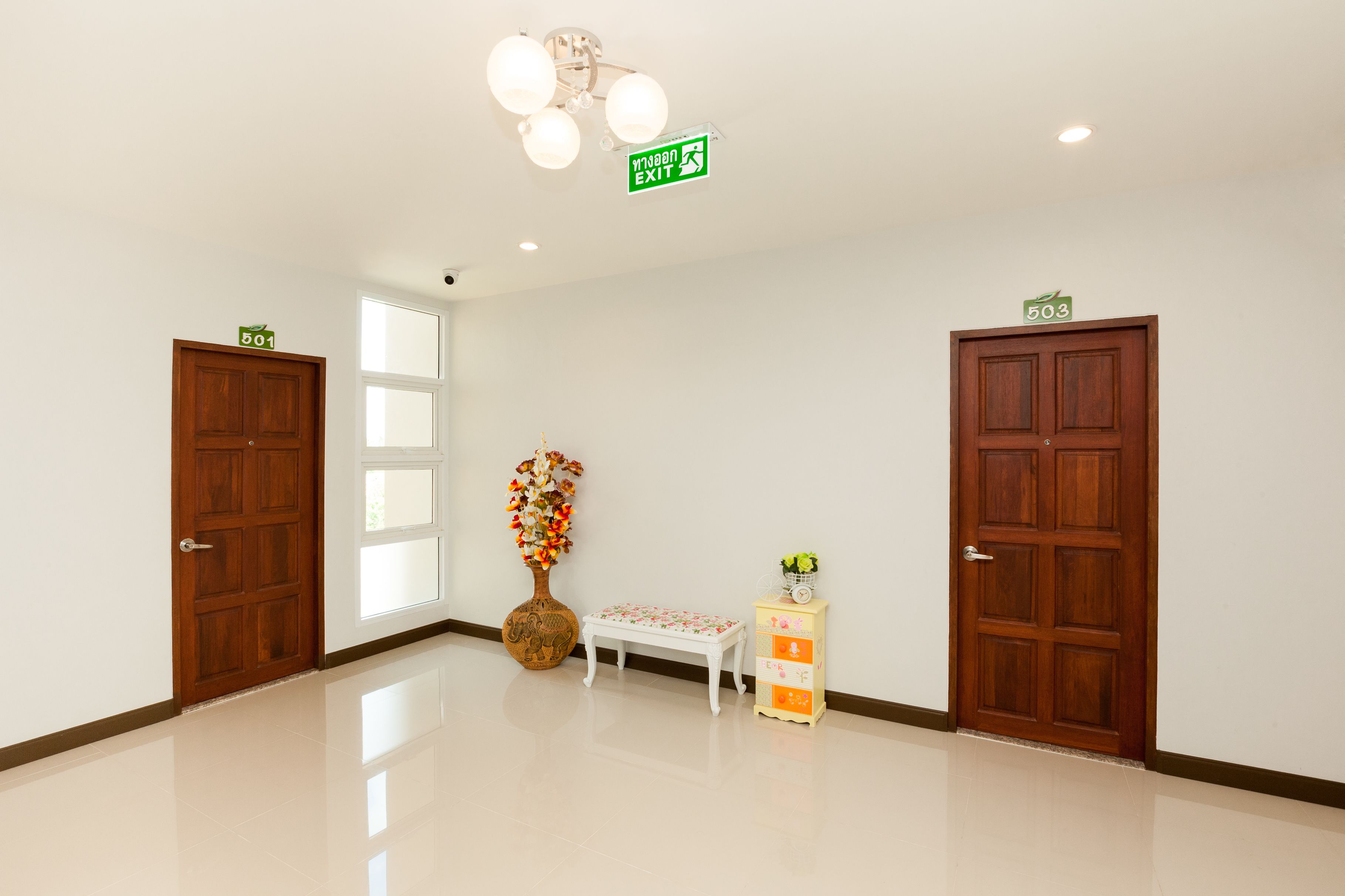 A clean, well-lit hallway with two wooden doors, a small bench, and a decorative vase.