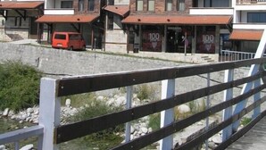 Un hôtel à plusieurs étages doté de balcons, un véhicule rouge garé devant, et un mur en pierre.