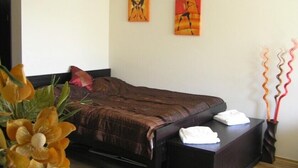 Une chambre à coucher comprenant un lit, une table de chevet, deux œuvres d’art murales et un vase décoratif contenant des branches.