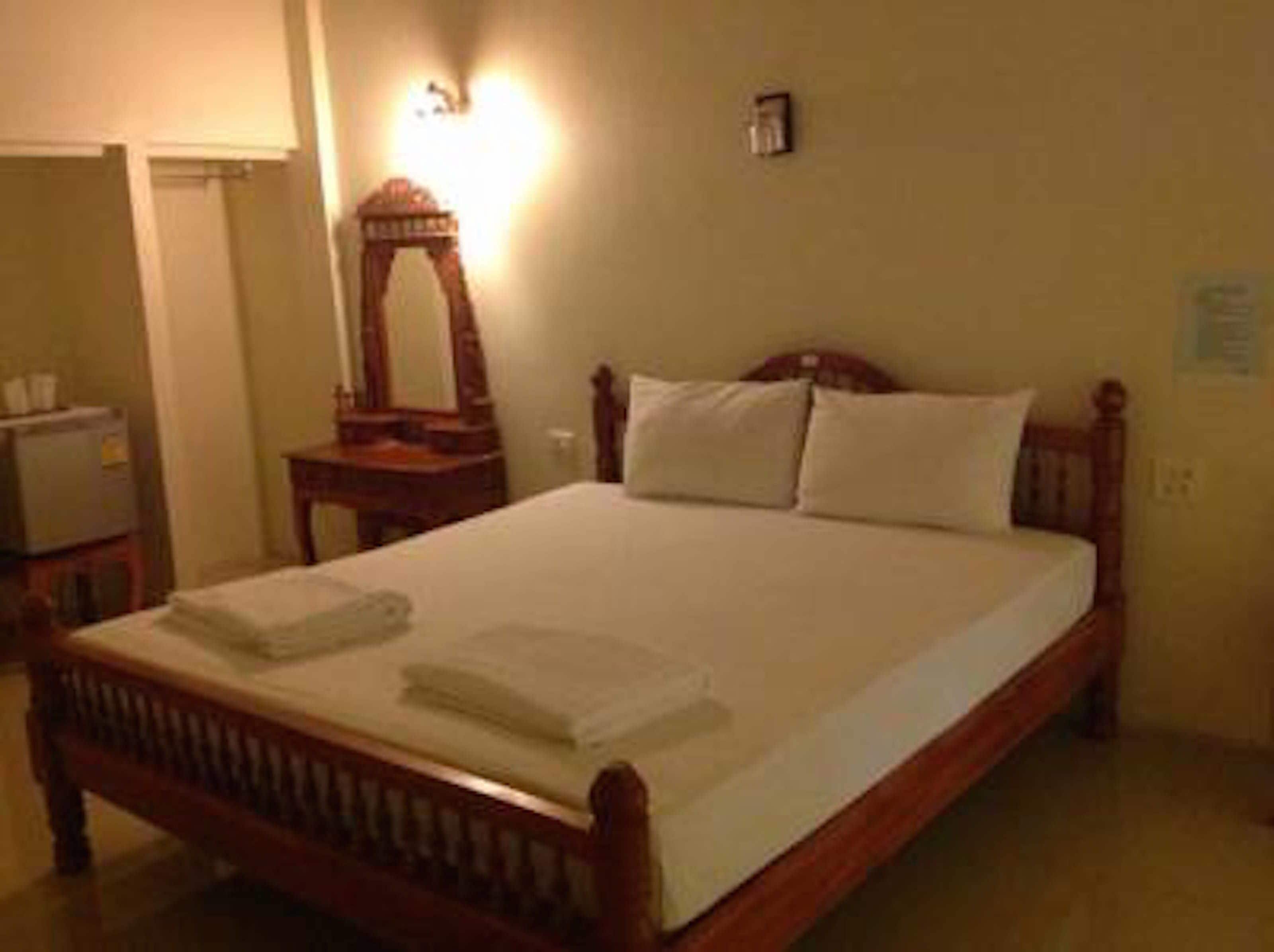 A neatly made bed with white linens and pillows, a wooden headboard, and a nightstand with a mirror.