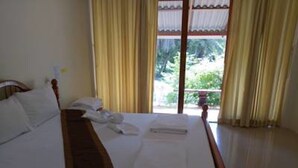 A hotel room with a bed, a wooden headboard, a window with curtains, and a view of greenery outside. - River Park Resort (Yan Ta Khao)