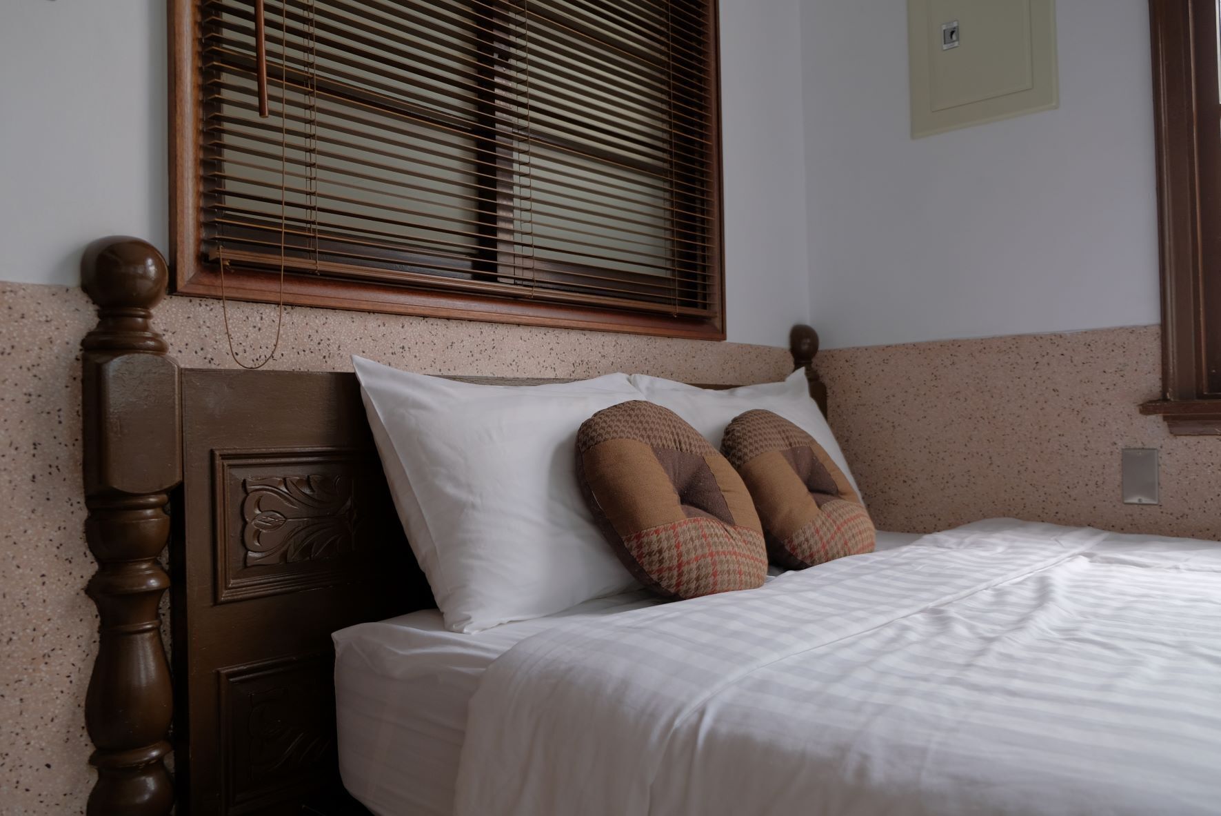 A neatly made bed with white bedding, a wooden headboard with carved details, and two patterned pillows.