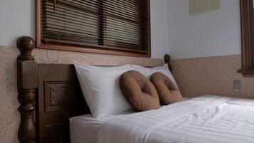 A neatly made bed with white bedding, a wooden headboard with carved details, and two patterned pillows.