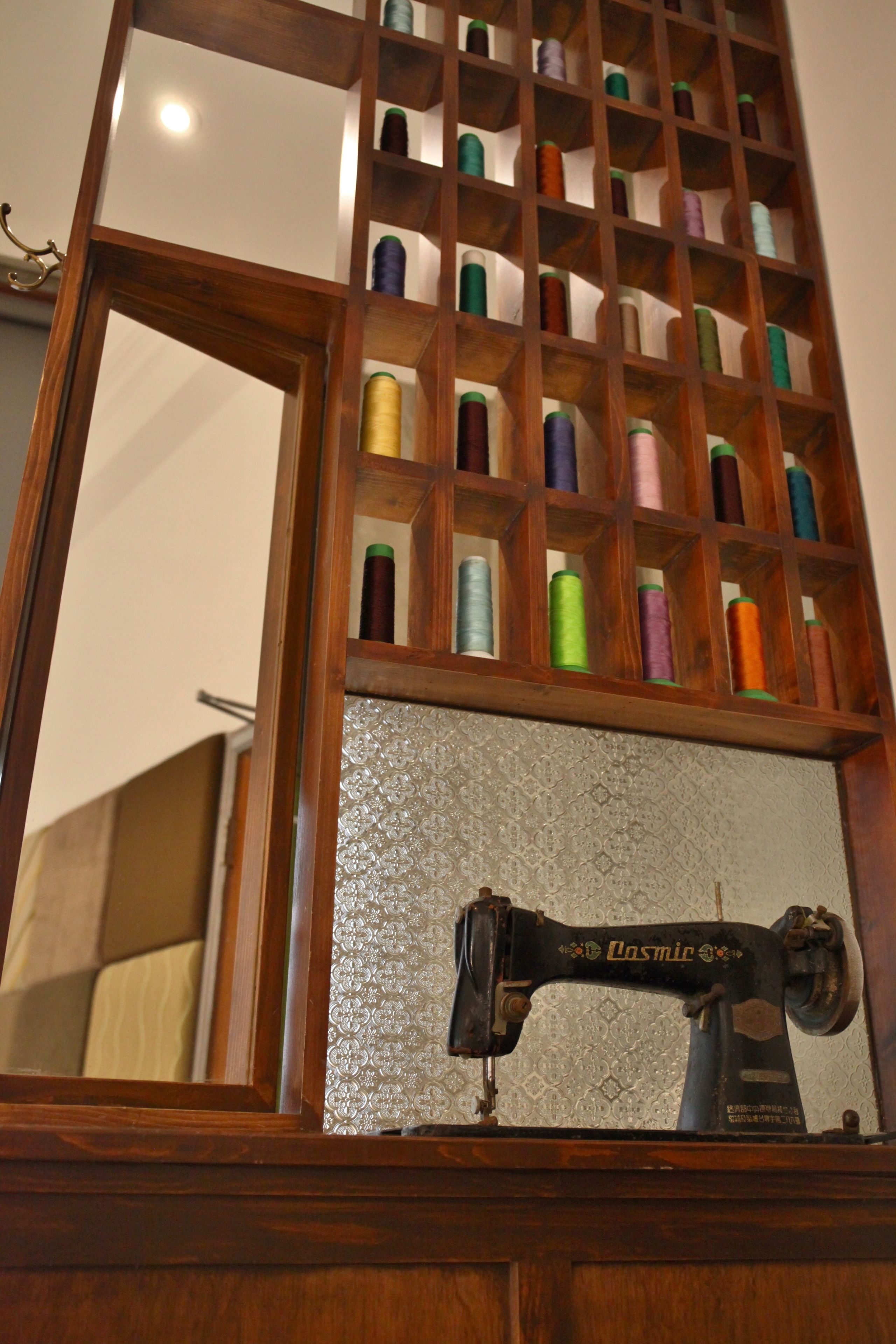 A wooden spool rack with various colored spools of thread, a vintage sewing machine, and a mirror reflecting part of the room.