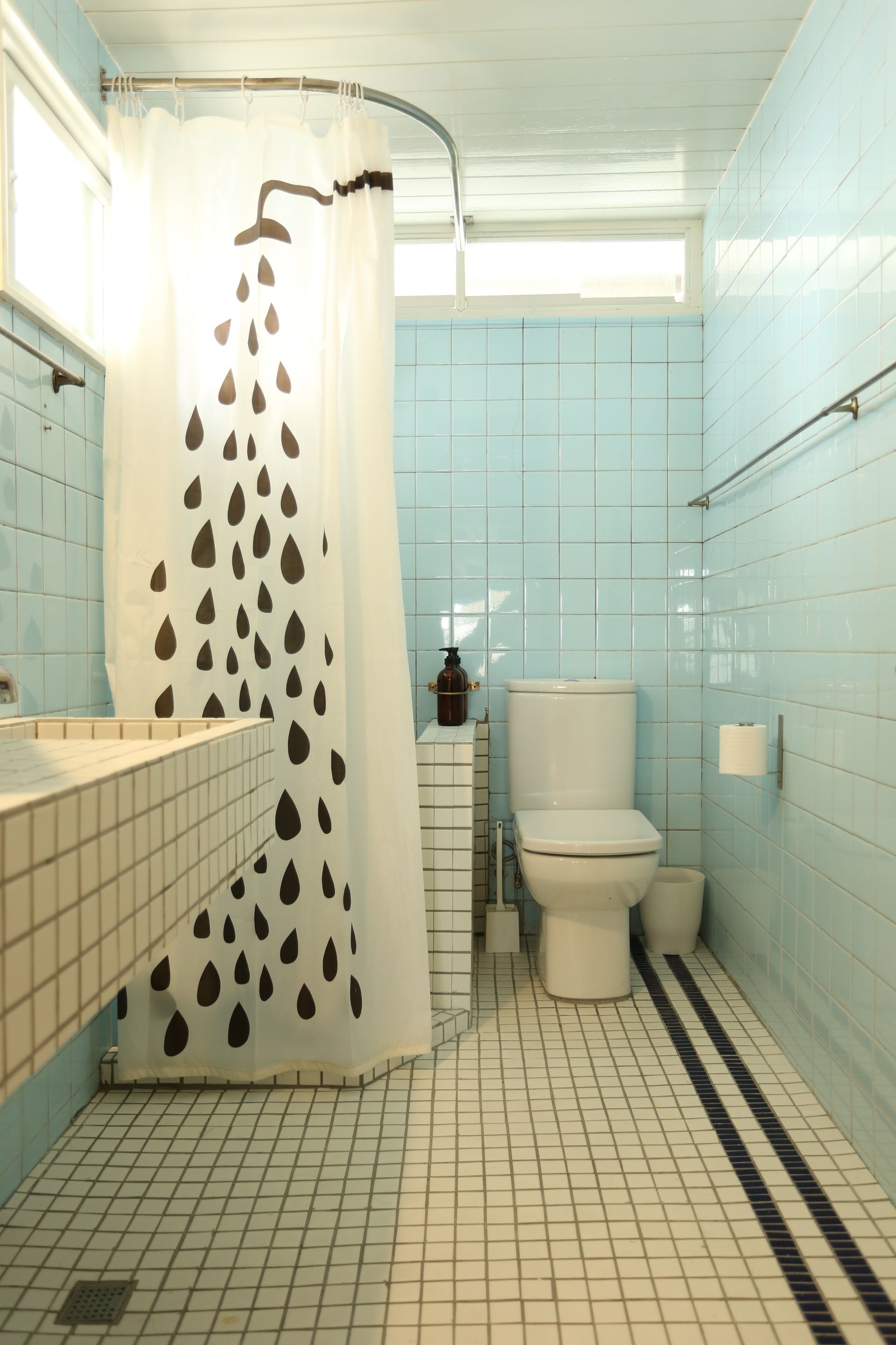 Een badkamer met douchegordijn, toilet en betegelde wanden.