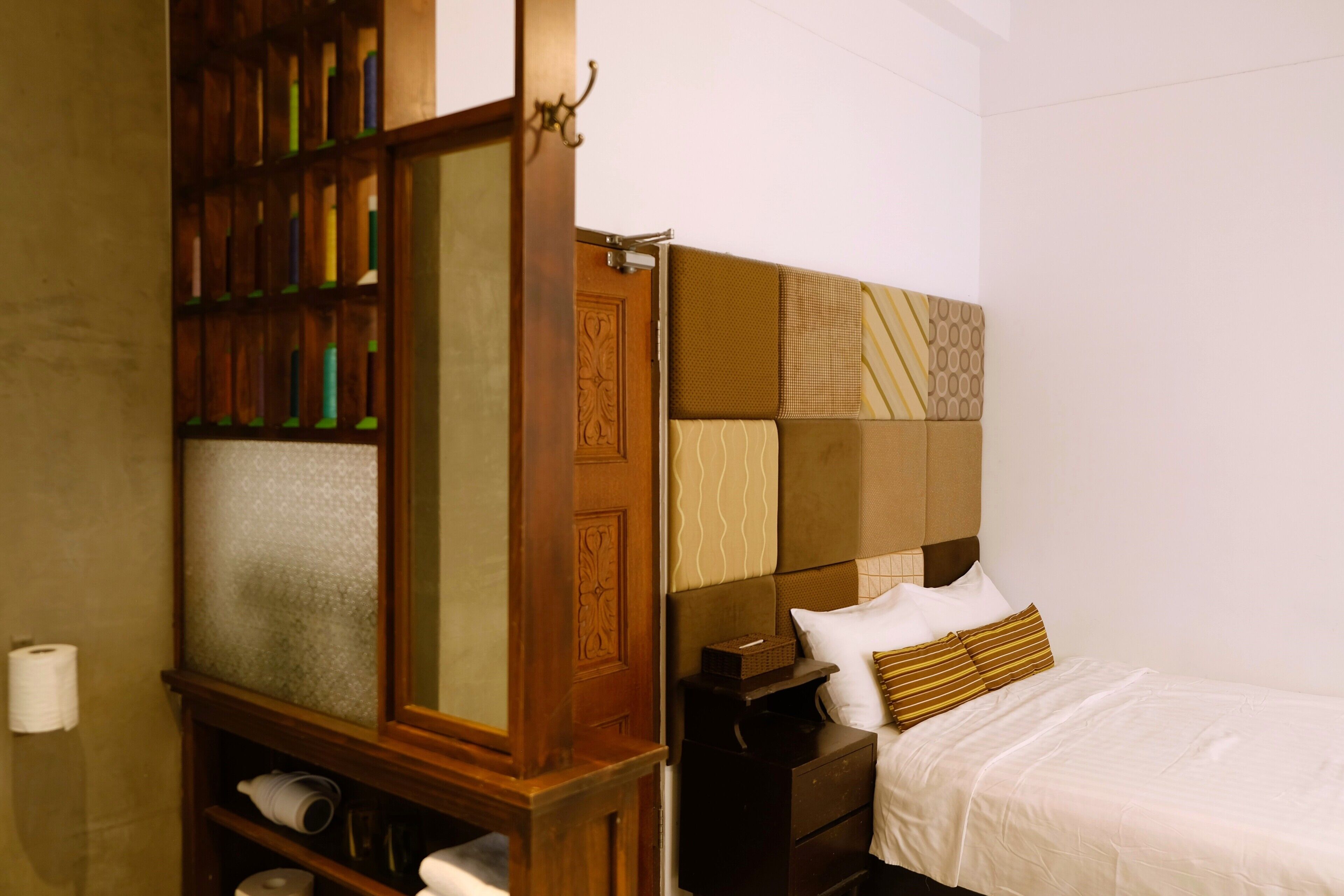 Habitación de hotel con un armario de madera, una cama con ropa de cama blanca y un cabecero con paneles estampados.