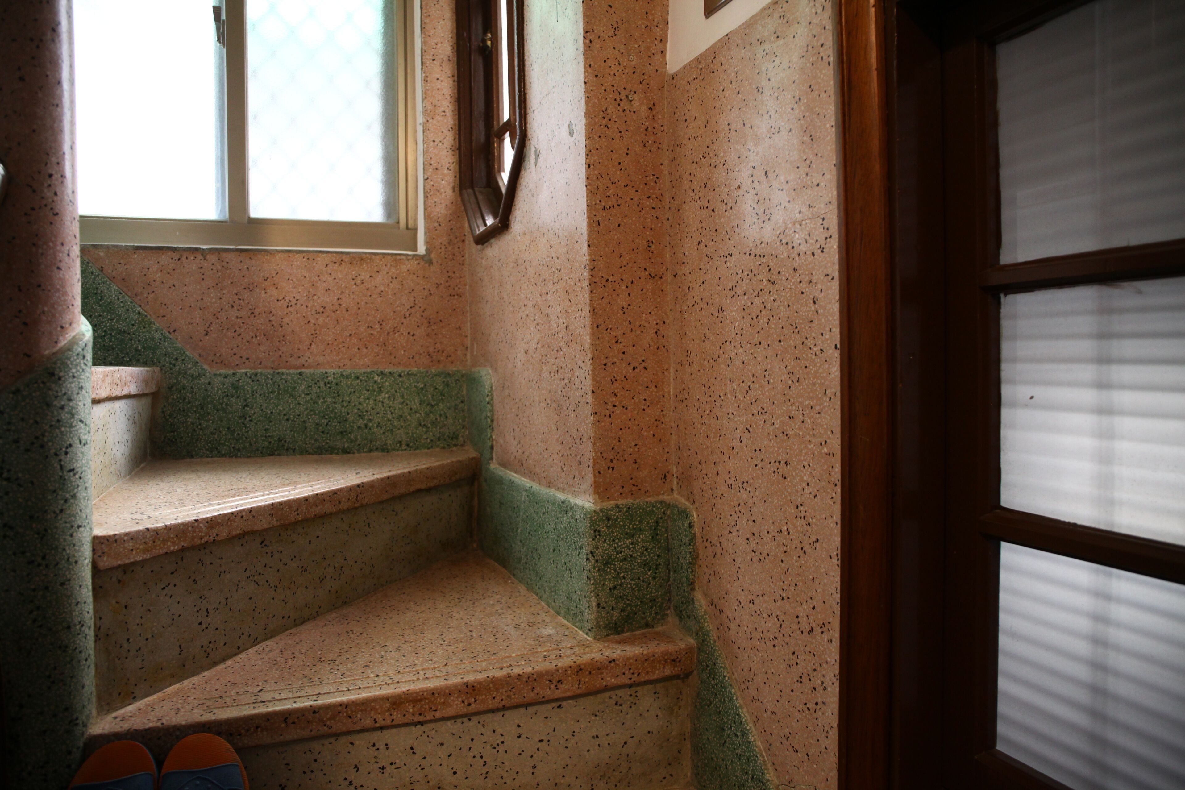 Unos escalones con borde verde, una ventana con persianas y una puerta con panel de vidrio satinado.