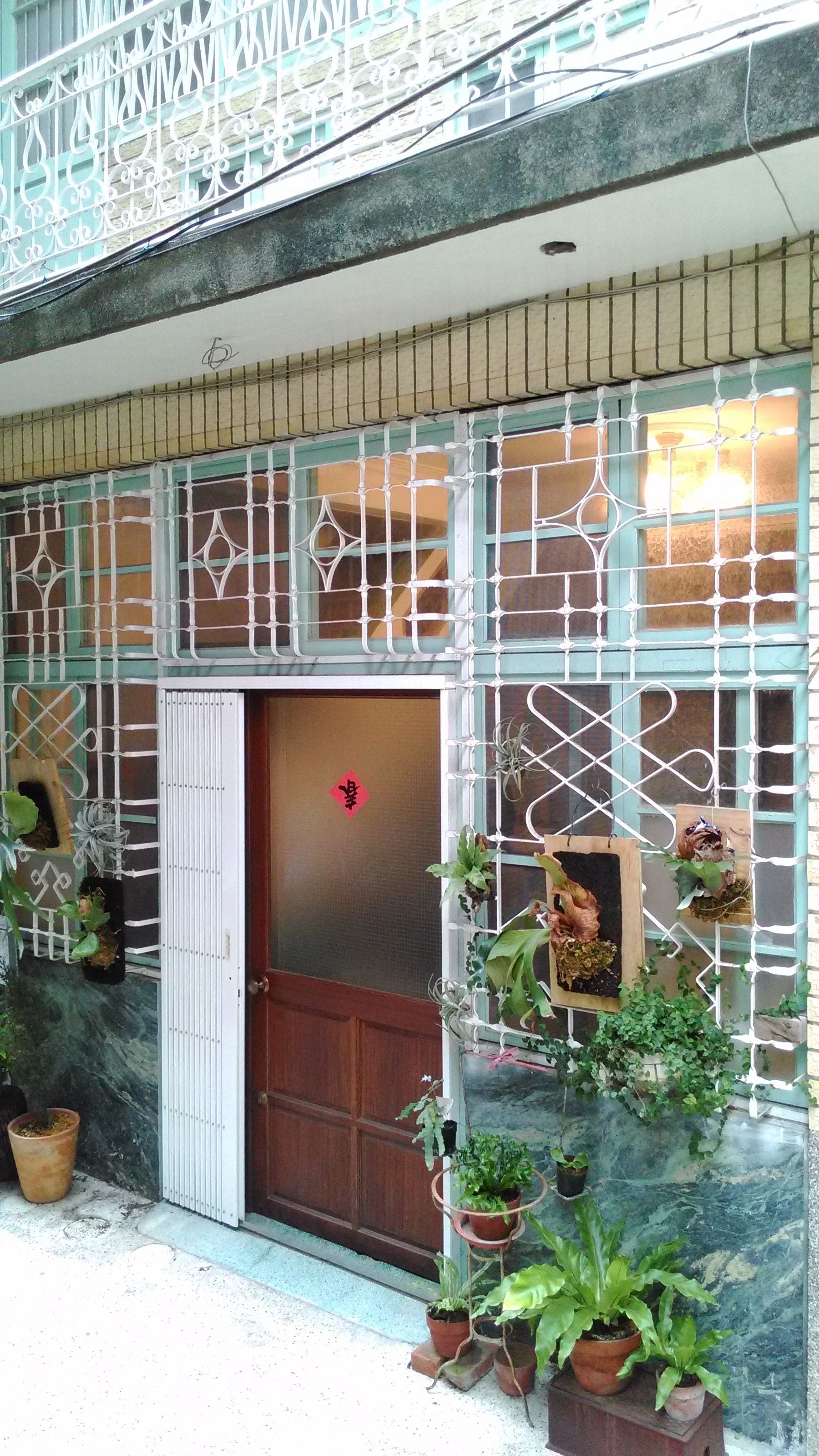 Fachada de un edificio con puerta de madera, barandillas decorativas de metal y plantas en macetas.