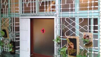 Fachada de un edificio con puerta de madera, barandillas decorativas de metal y plantas en macetas.