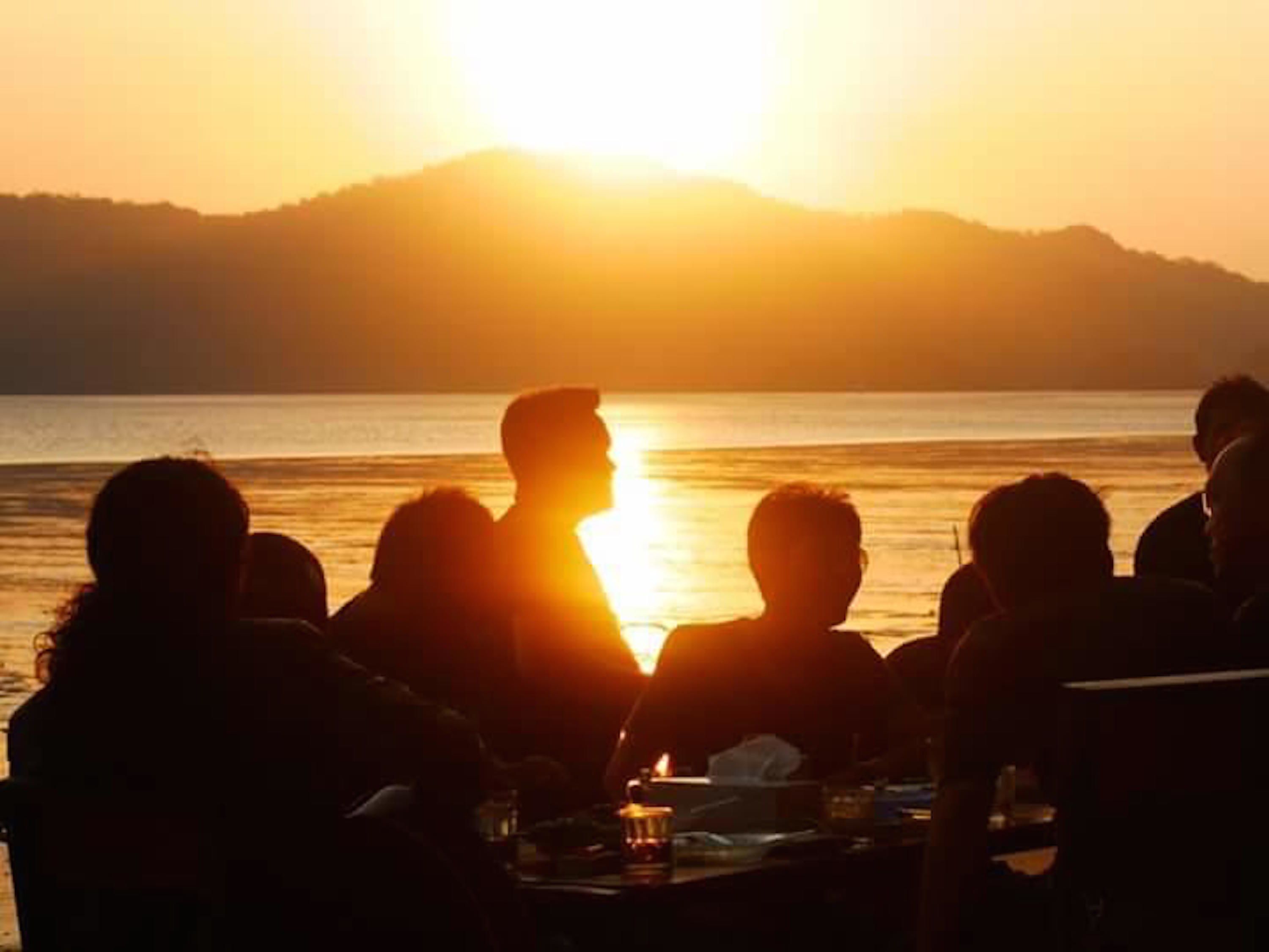 Un grupo de personas sentadas a una mesa junto al agua al atardecer.