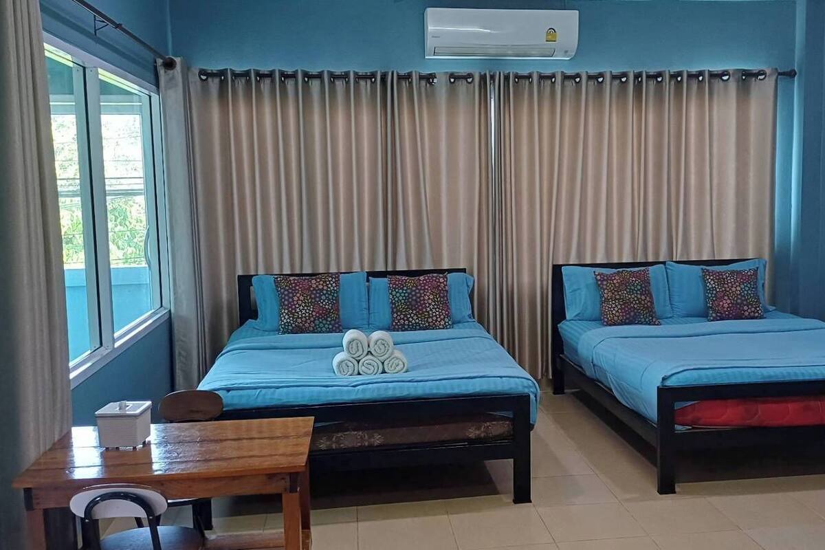 Une chambre avec deux lits, une petite table, une chaise, un bureau et une fenêtre avec des rideaux.