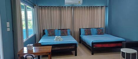 A room with two beds, a small table, a chair, a desk, and a window with curtains.
