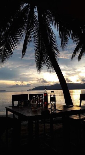 Una mesa con botellas y vasos, con vistas a una masa de agua y palmeras al frente.