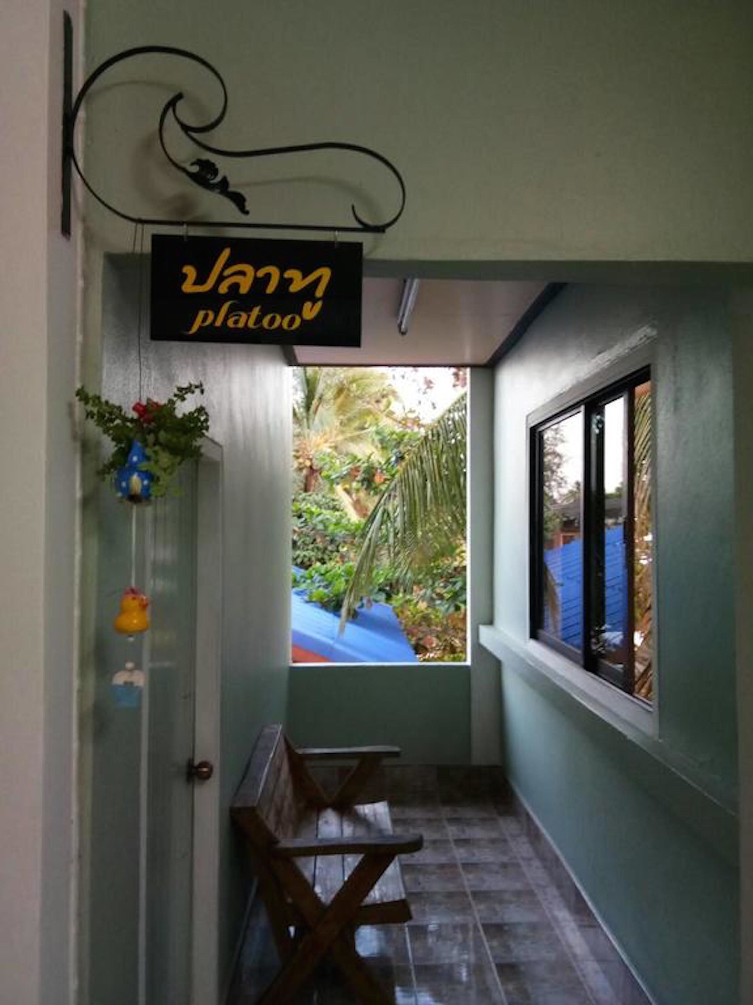 A narrow hallway with a bench, a window with a view of greenery, and a sign reading "Vanny plazao".