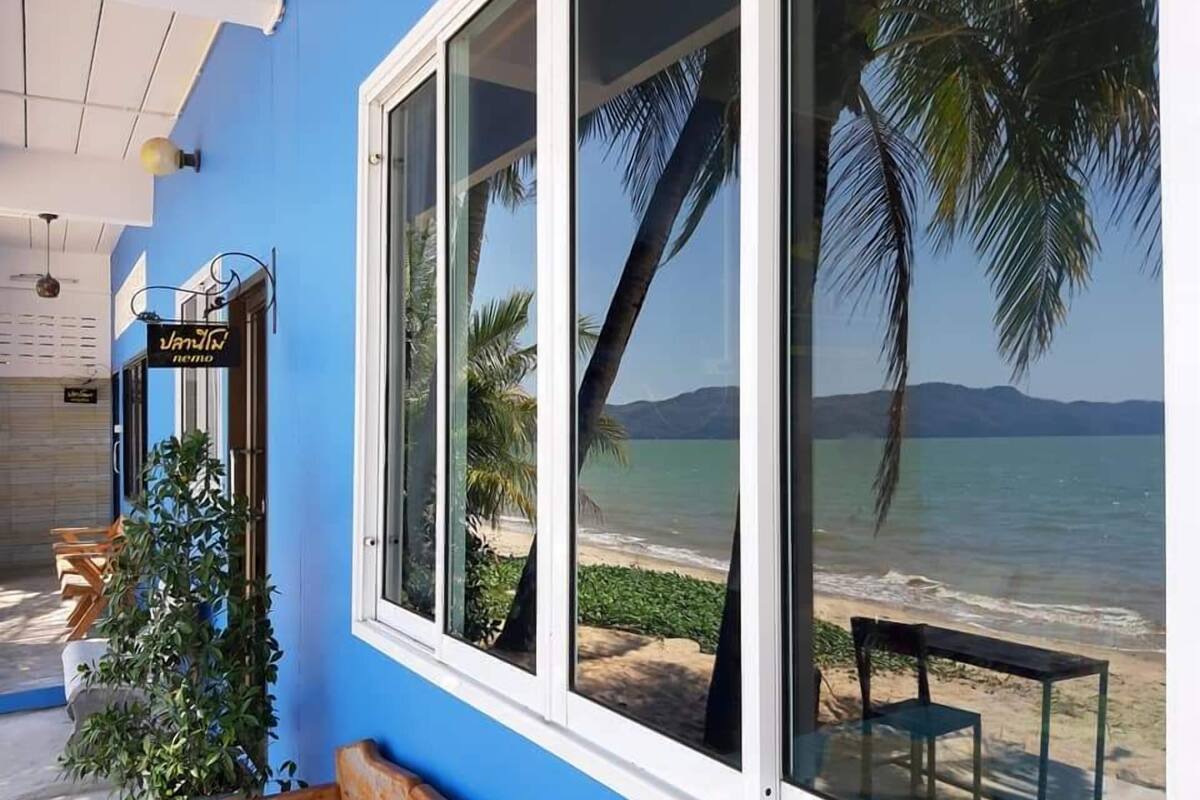 Un bâtiment situé sur la côte, doté de grandes fenêtres qui offrent une vue sur la mer et les palmiers.
