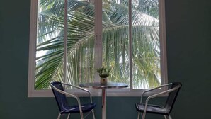 Una habitación con un ventanal grande, dos sillas y una mesita con una planta.