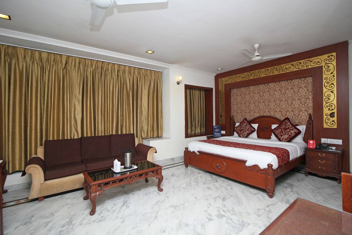 A hotel room with a large bed, a sofa, a coffee table, and a nightstand.