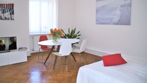 Une chambre moderne équipée d’une table à manger, de chaises, d’un téléviseur, d’un lit et d’une fenêtre avec des rideaux.
