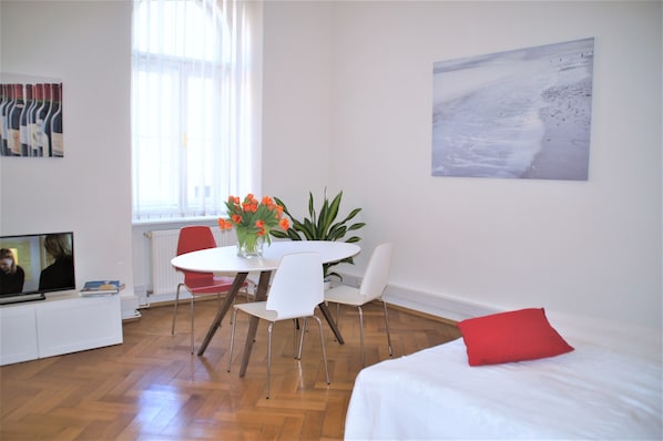 A modern room with a dining table, chairs, a TV, a bed, and a window with curtains.