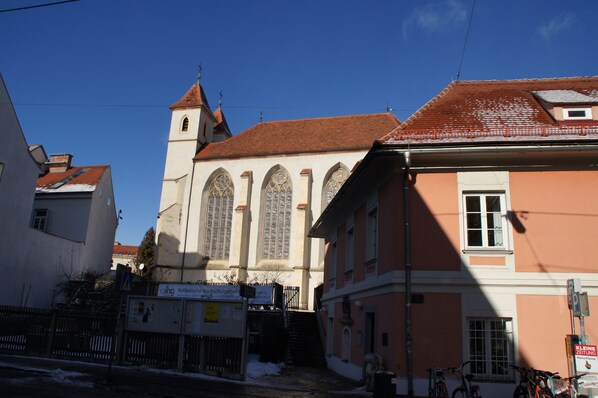 A building with a tower, arched windows, and a red-tiled roof. - Charming apartment in an ideal location (Graz)