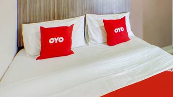 A bed with white bedding and two red pillows with the word "OYO" on them.