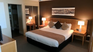 A hotel room with a large bed, two bedside tables with lamps, a wardrobe, and a mirror. - Pier One (Urangan)