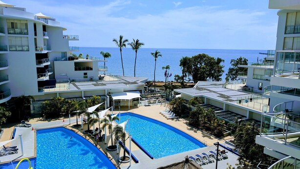 A resort with two swimming pools, palm trees, and a view of the ocean. - Pier One (Urangan)