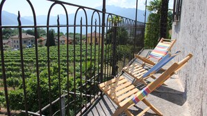 Ein Balkon mit zwei Holzliegen, einem schmiedeeisernen Geländer und Blick auf einen Weinberg.