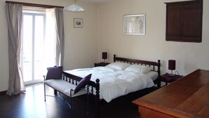 Ein Schlafzimmer mit einem großen Bett, einem Nachttisch aus Holz, einem Schreibtisch und einem Fenster mit Vorhängen.