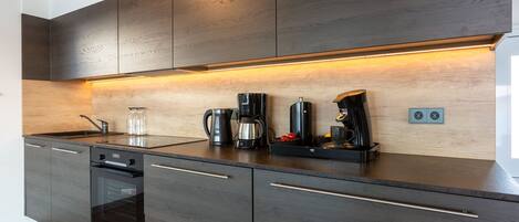 A modern kitchen with dark wood cabinets, a built-in oven, and a coffee station.