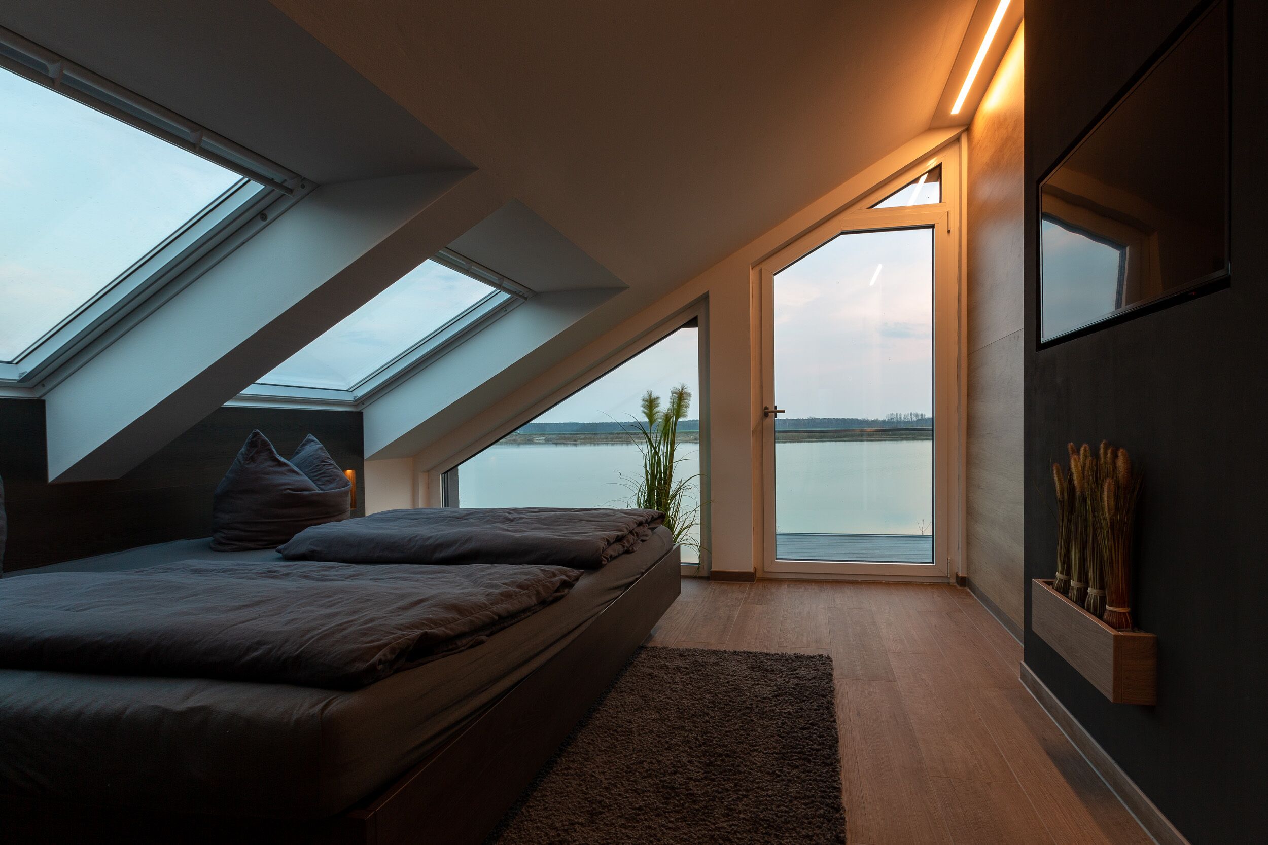 A bedroom with a skylight, a bed, a view of the water, and a plant on the wall.