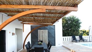 An outdoor patio with a dining table and chairs, a pool, and a covered seating area with a wooden ceiling.
