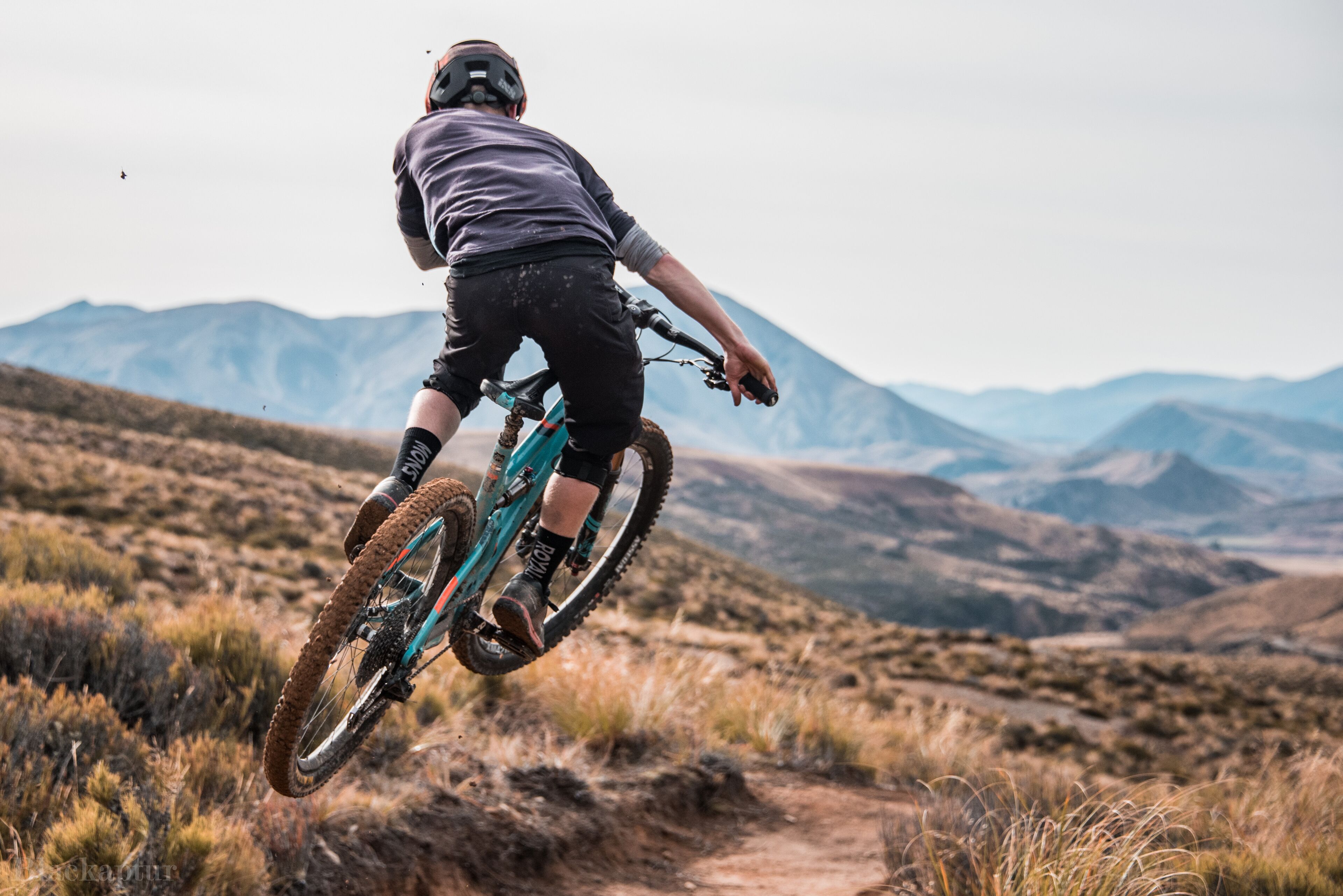 A person riding a mountain bike on a dirt trail with a mountainous landscape in the background.