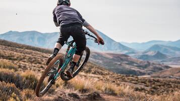 A person riding a mountain bike on a dirt trail with a mountainous landscape in the background.
