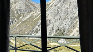 A window view of a mountainous landscape with a metal railing in the foreground. - Porters Lodge (Castle Hill)
