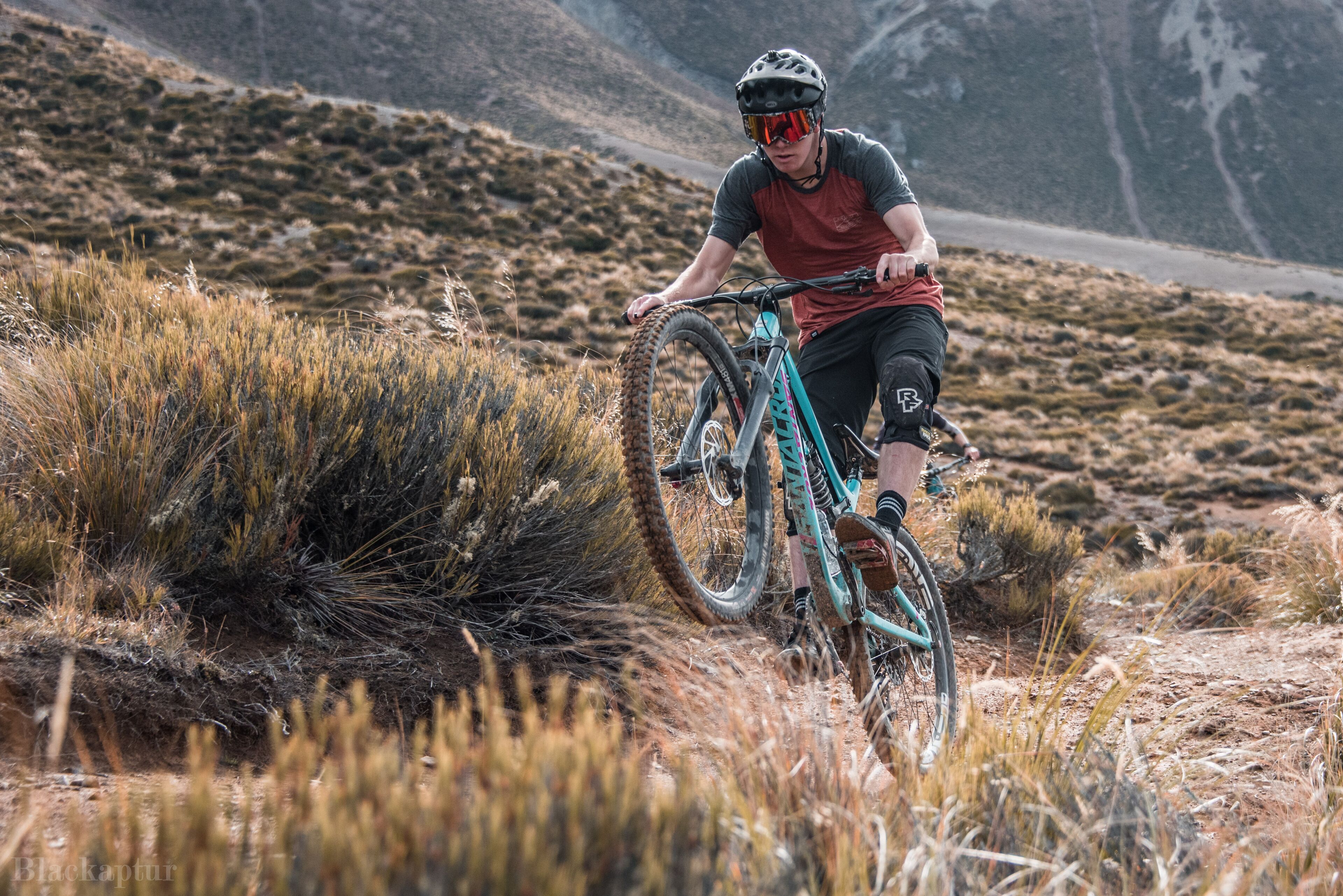 A mountain biker on a trail with sparse vegetation and a mountainous backdrop.