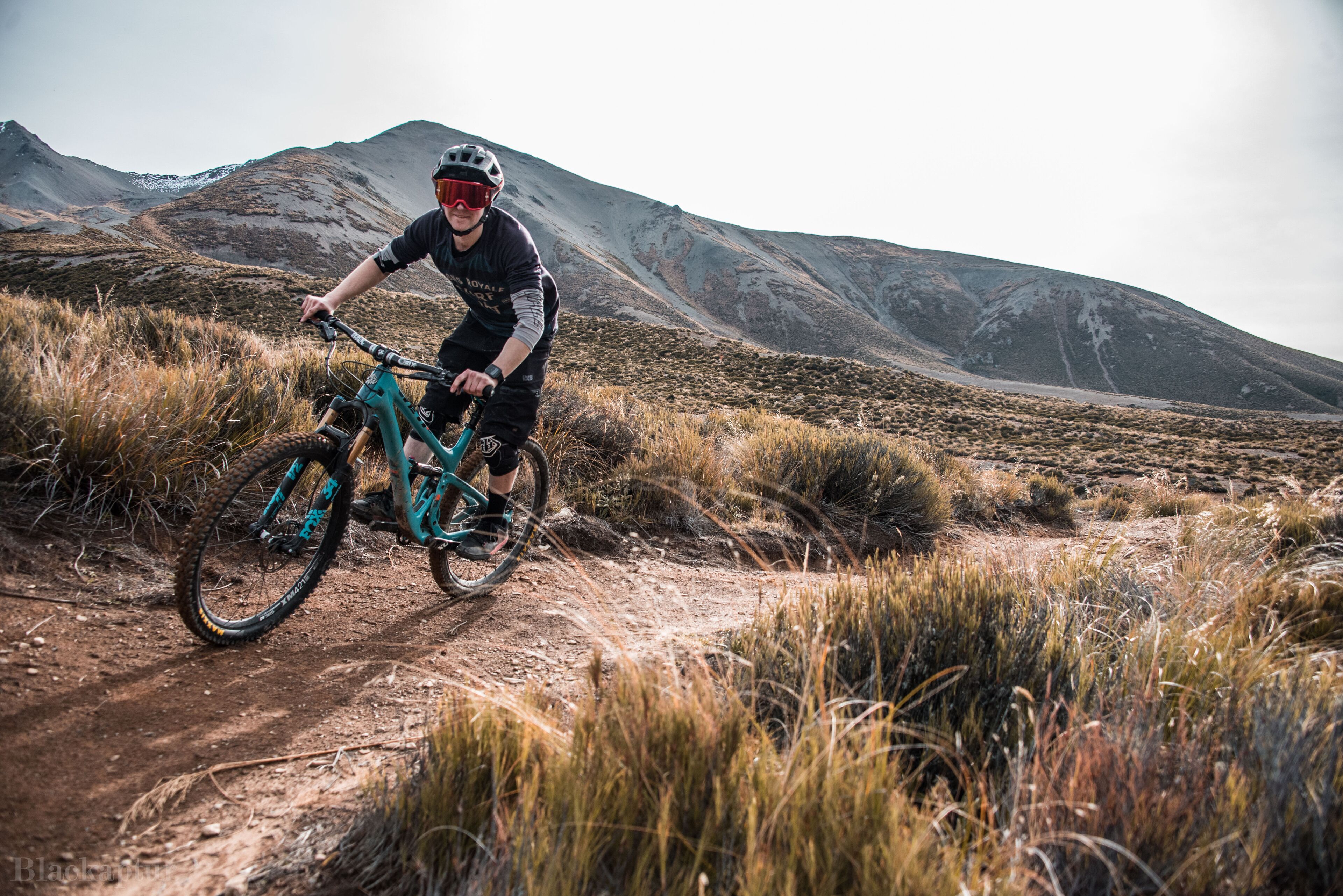 A mountain biker on a dirt trail with a mountainous backdrop.
