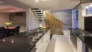 A modern kitchen with a black countertop, stainless steel appliances, and a wooden staircase. - 15 Melbourne by Staysouth (Queenstown)