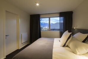 Une chambre d’hôtel avec un grand lit, une fenêtre avec des rideaux, un radiateur et une vue sur les montagnes.