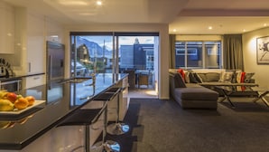 A modern kitchen with a bar area, a dining space with a view, and a living area with a sofa and coffee table. - 15 Melbourne by Staysouth (Queenstown)