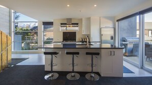 A modern kitchen with a central island, bar stools, and a view of a mountain landscape. - 15 Melbourne by Staysouth (Queenstown)