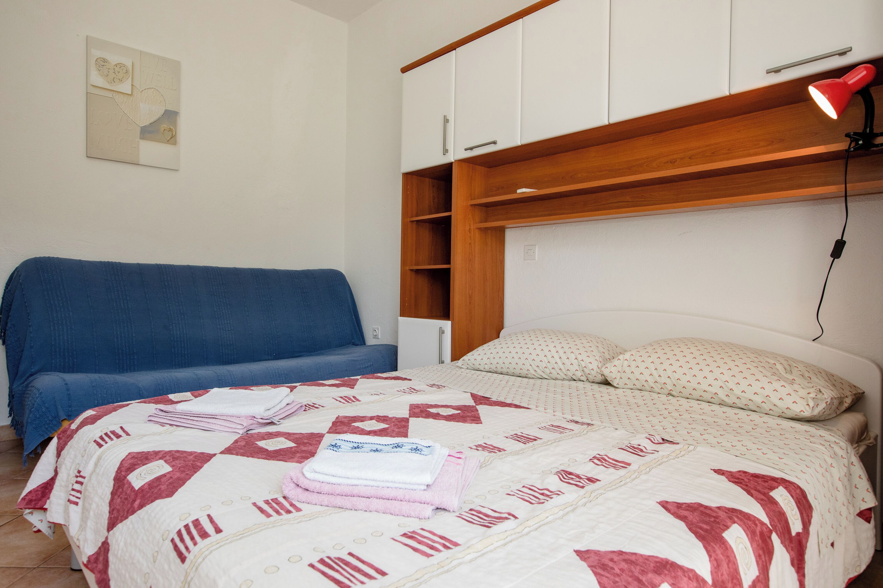 A bedroom with a bed, a blue sofa, a wooden headboard, and a wall-mounted lamp.