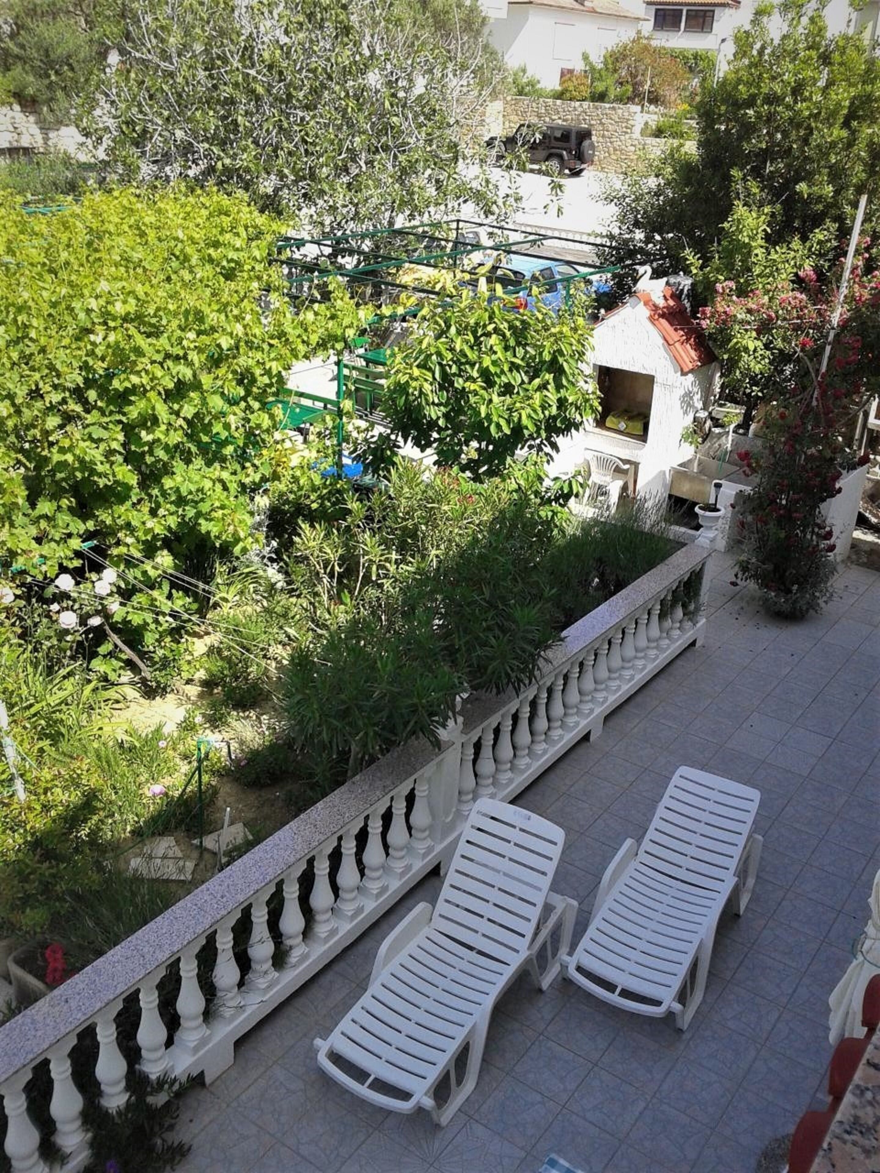 A terrace with white lounge chairs, a stone balustrade, and lush greenery.