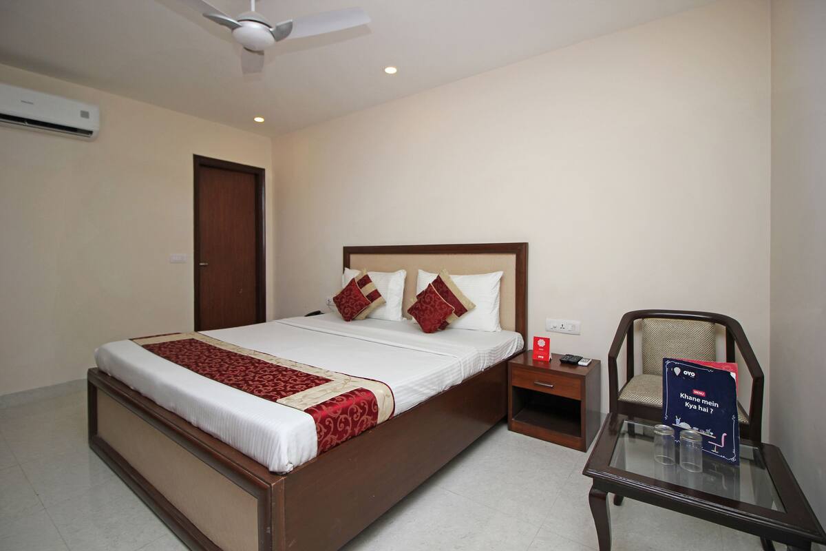 A hotel room with a large bed, a nightstand, a chair, and a table with a sign.