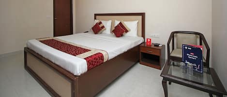 A hotel room with a large bed, a nightstand, a chair, and a table with a sign.